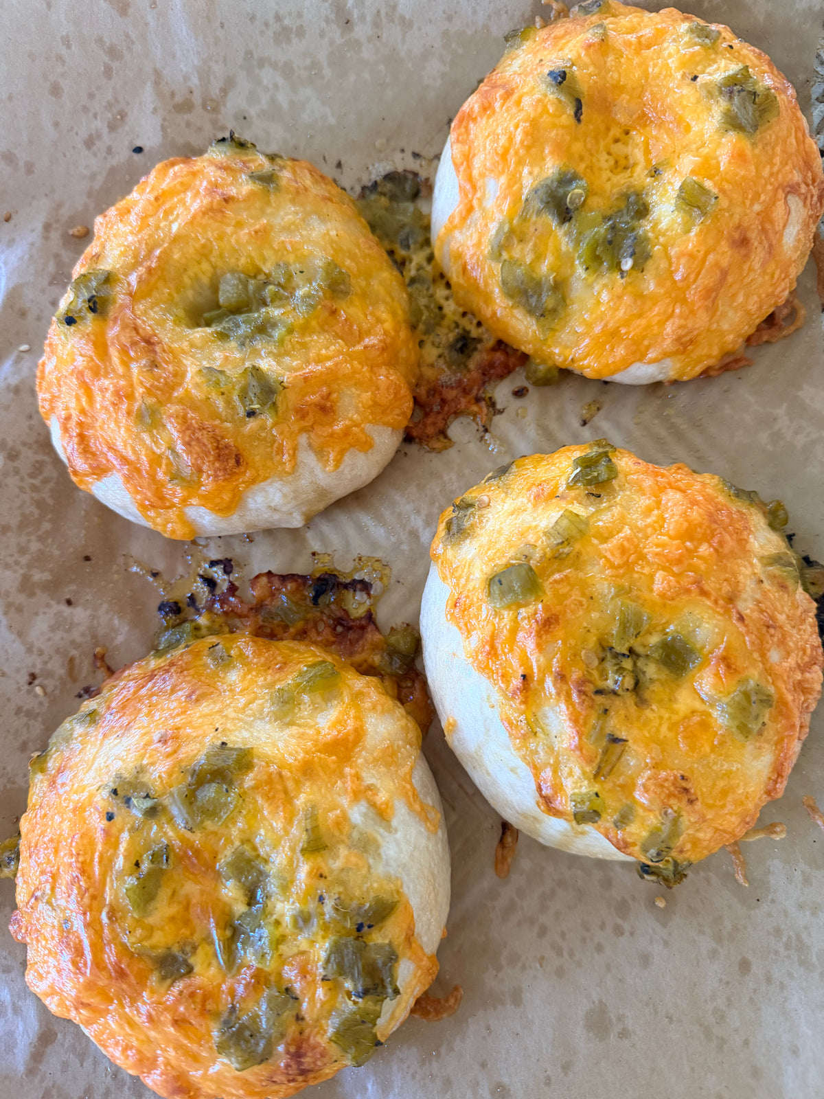Four beagles with cheese and green peppers on a baking tray.
