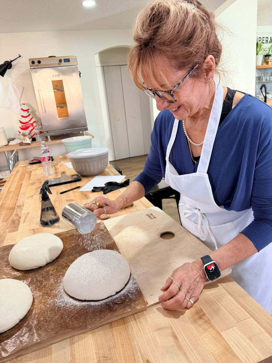 Person in a kitchen preparing dough on a wooden counter.